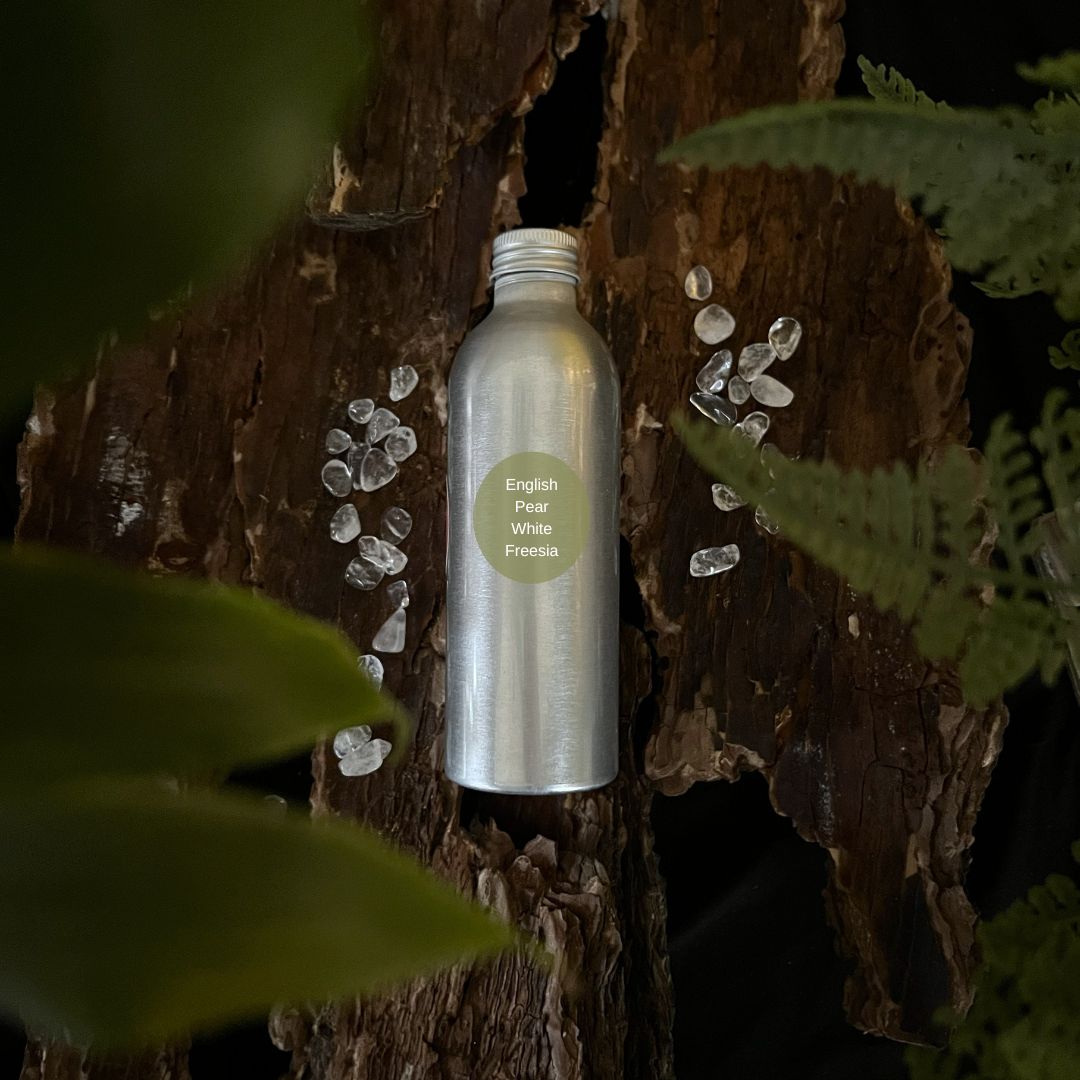 Aluminium English Pear and White Freesia room spray refill bottle on a tree trunk with leaves in the foreground
