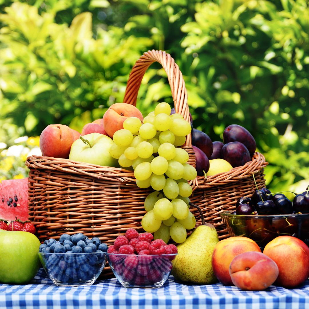 Basket and bowls of fruits on a table with a garden background