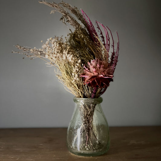 Glass vase with dried flowers on a wooden surface and grey background