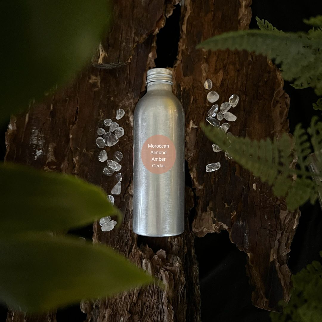 Aluminium Moroccan Almond, Amber and Cedar room spray refill bottle on a tree trunk with leaves in the foreground