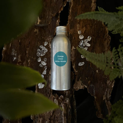 Aluminium Orange, Clove & White Woods reed diffuser refill bottle on a tree trunk with leaves in the foreground