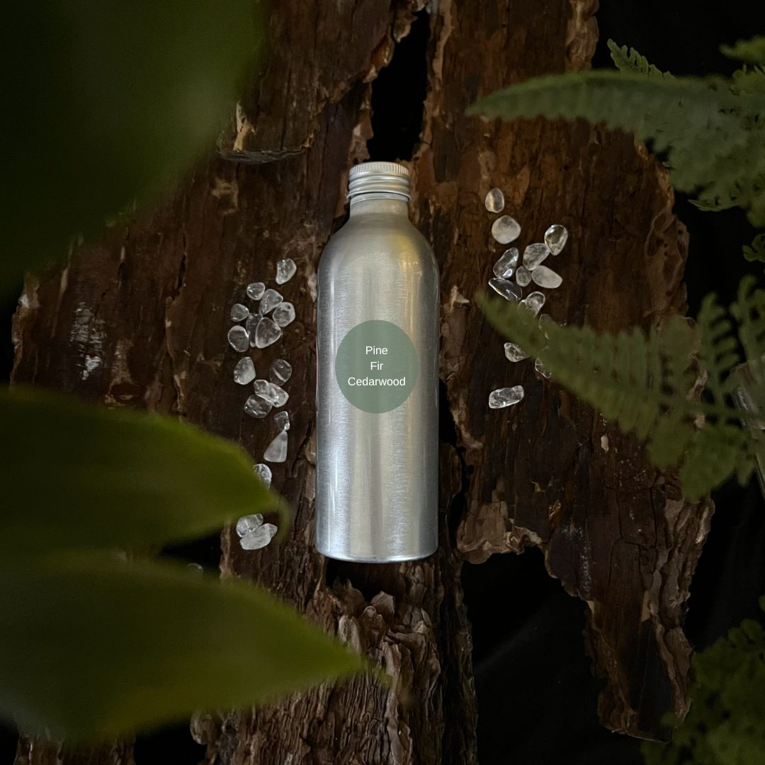 Aluminium Pine, Fir and Cedarwood reed diffuser refill bottle on a tree trunk with leaves in the foreground