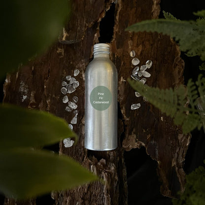 Aluminium Pine, Fir and Cedarwood reed diffuser refill bottle on a tree trunk with leaves in the foreground