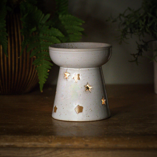 Ceramic wax and oil burner with star designs on a wooden surface